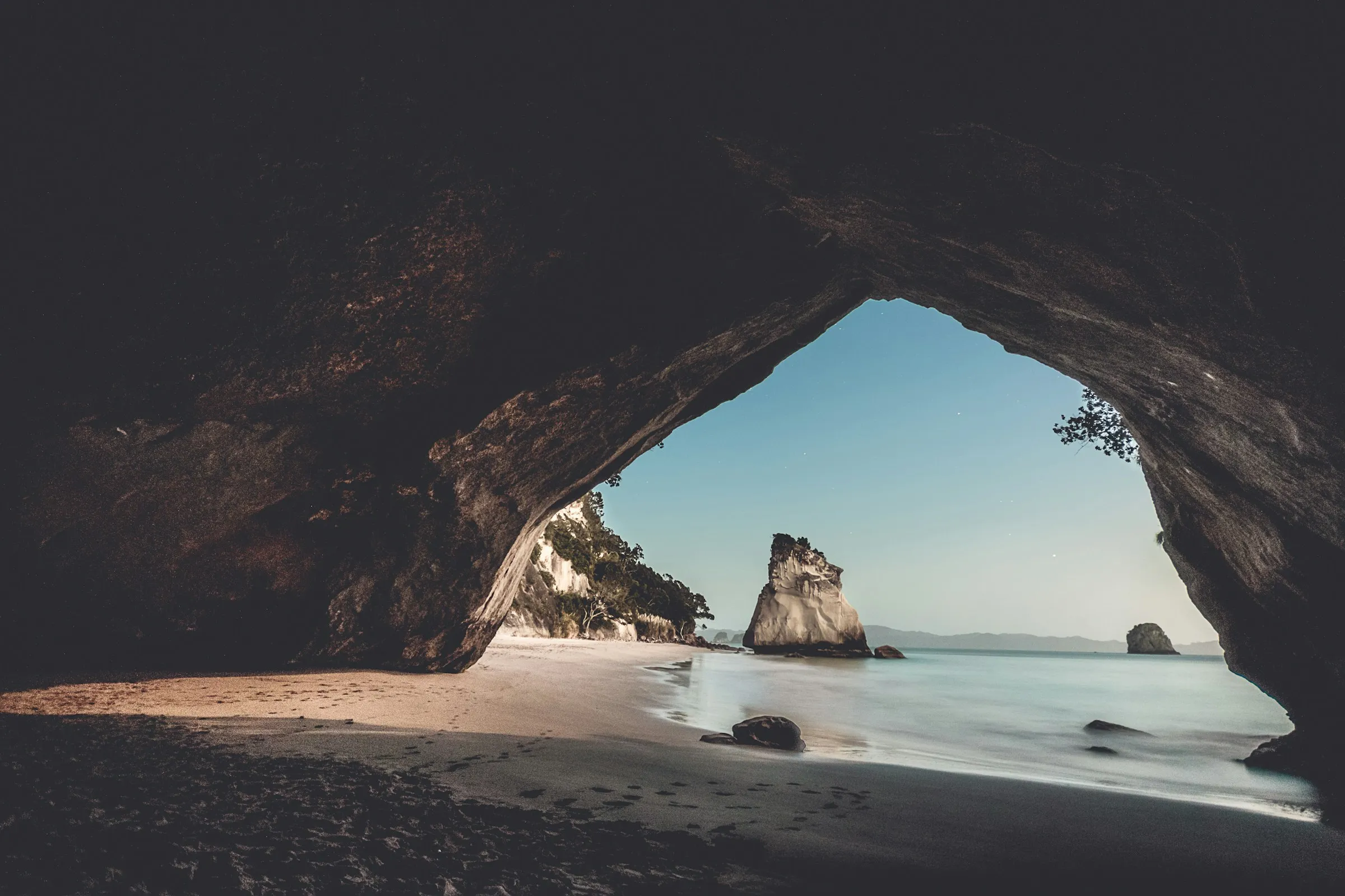 A dark rock arch frames a sea stack and still water at dawn