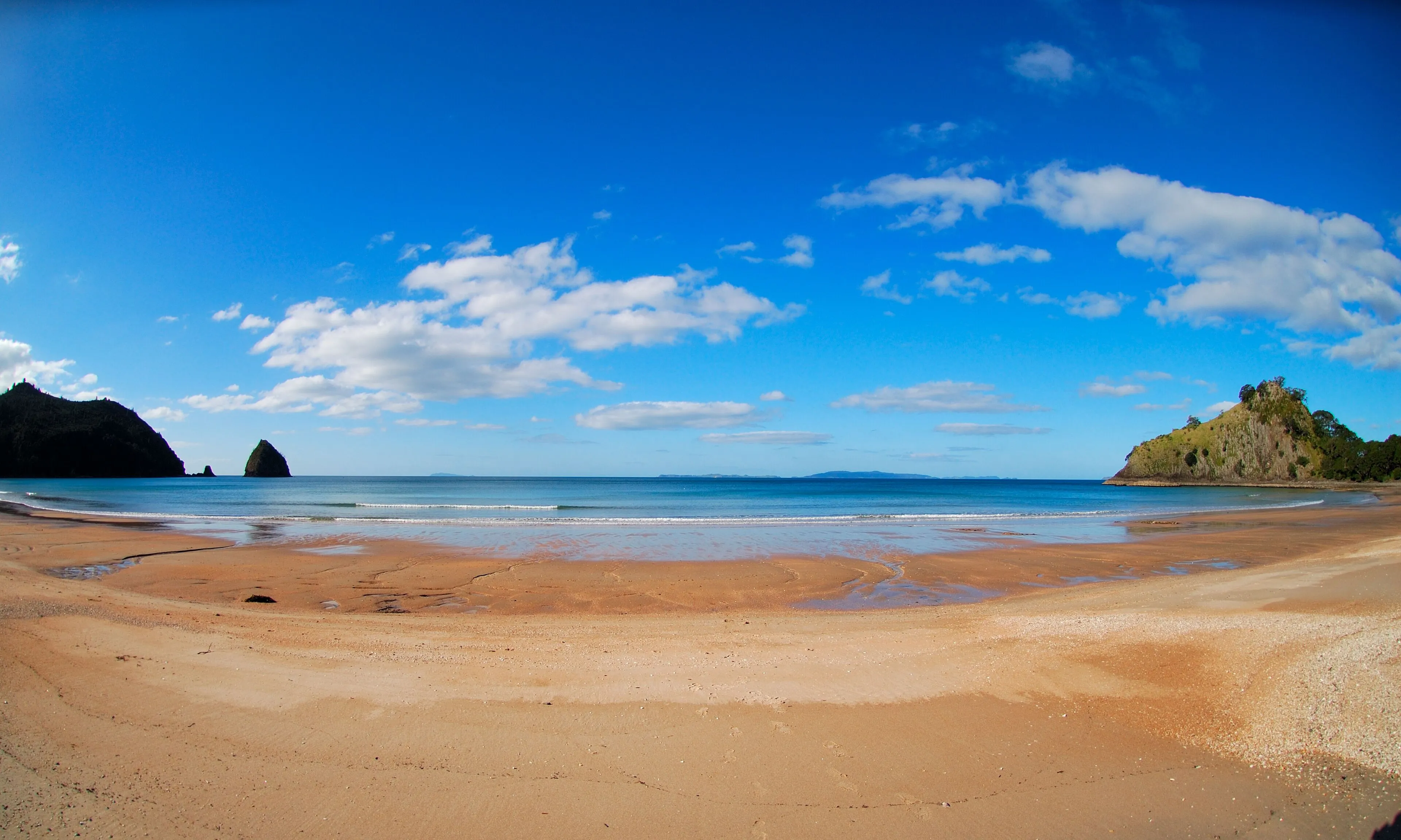 New Chums Beach, a sheltered bay with orange sand and rocky islands under a clear blue sky